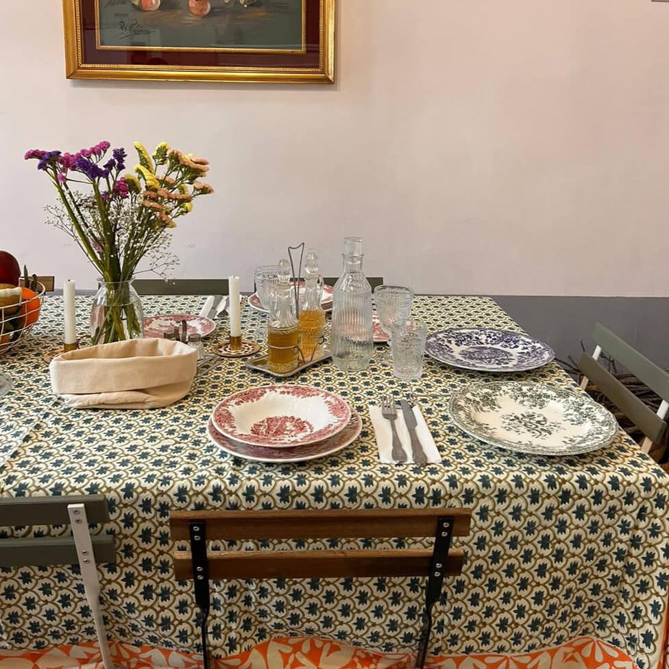 Et dug/sengetæppe med et grønt blomstermønster i midten og en orange og grøn kant