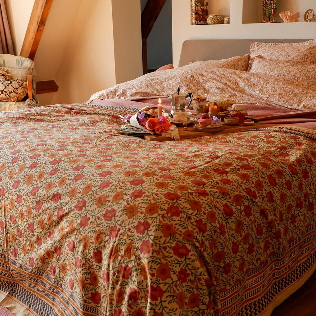 Et dug/sengetæppe med et beige blomstermønster i midten og en beige/grå kant