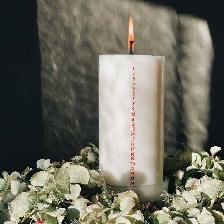 Hvidt kalenderlys med røde tal. Kalenderlyset består af 51% sojavoks og 49% stearin, og er derfor det tætteste, man kan komme på et soja-kalenderlys.