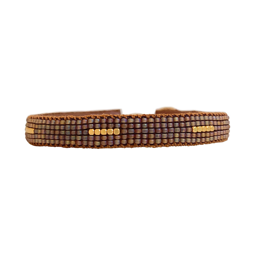Winter Stripe armbåndet fra IBU Jewels er et fint perlearmbånd med en farve som base, hvor der er en samling af 5 små guldperler i midten af armbåndet samt samlinger af perler på tværs af armbåndet. Armbåndet er lavet af eksklusive Miyuki-perler, som er håndsyet på blødt læder. Denne model er med brune perler som base.