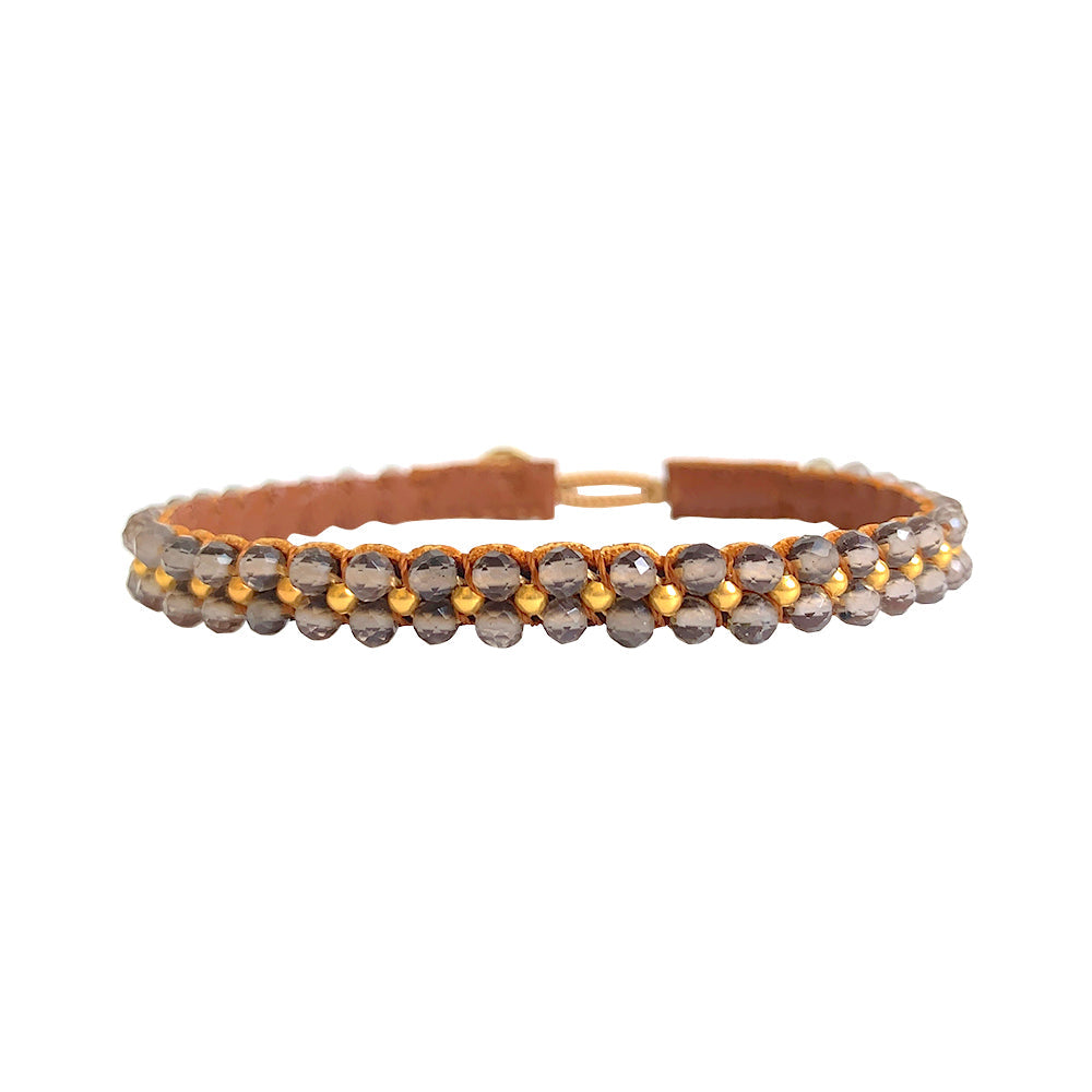 Bee armbåndet fra IBU Jewels er et enkelt armbånd, som primært består af perler med en enkelt guldperle imellem. 'Smokey Quartz' består af en base af grå sten. Hvis du tager armbåndet op i lyset vil perlerne vise sig fra forskellige vinkler.