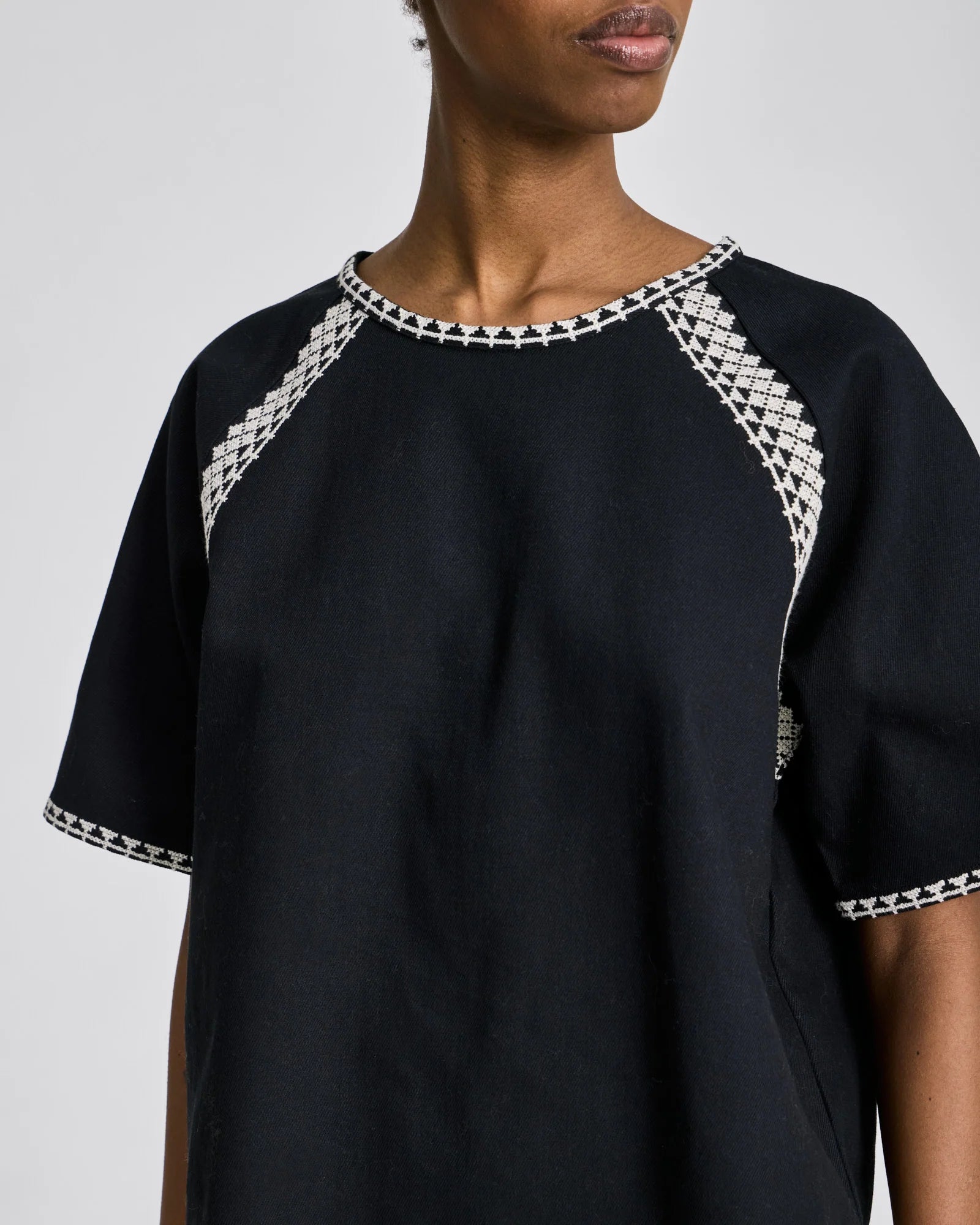 Detaljebillede af hvide broderi på sort Angie T-shirt i 100% økologisk bomuld.