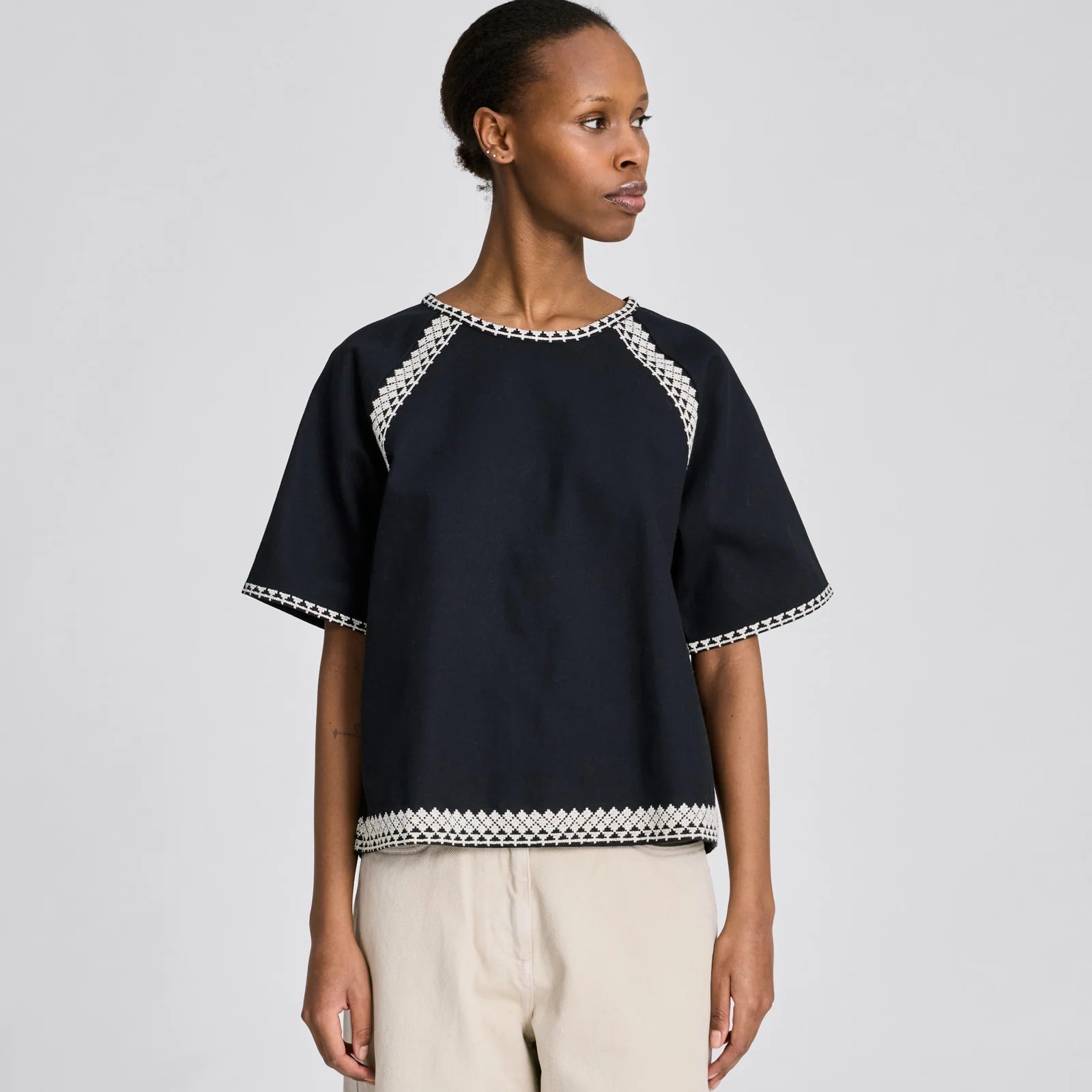 Forside af sort Angie T-shirt med hvidt broderi og nøglehulslukning i nakken.