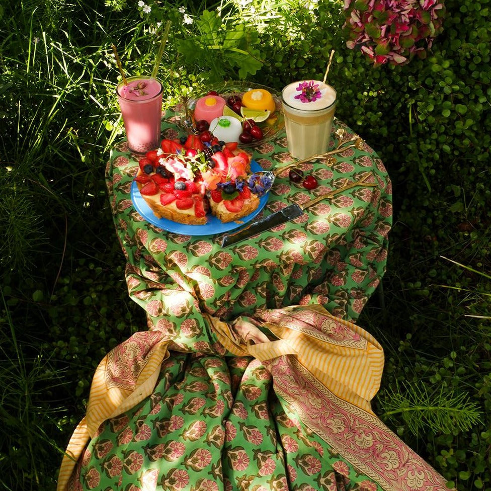 Et dug/sengetæppe med et grønt blomstermønster i midten og en lyserød og gul kant