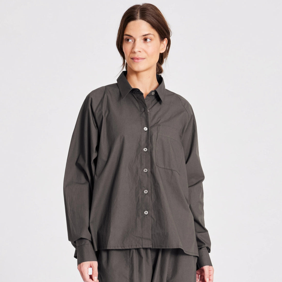 Bella er en lang skjorte med lange raglan ærmer, brystlomme samt knapper foran og på manchetter. Bella har plisseringer bagpå, slidser i siderne og er længere bagpå. Denne er i farven Beluga, som er en khaki/brun farve