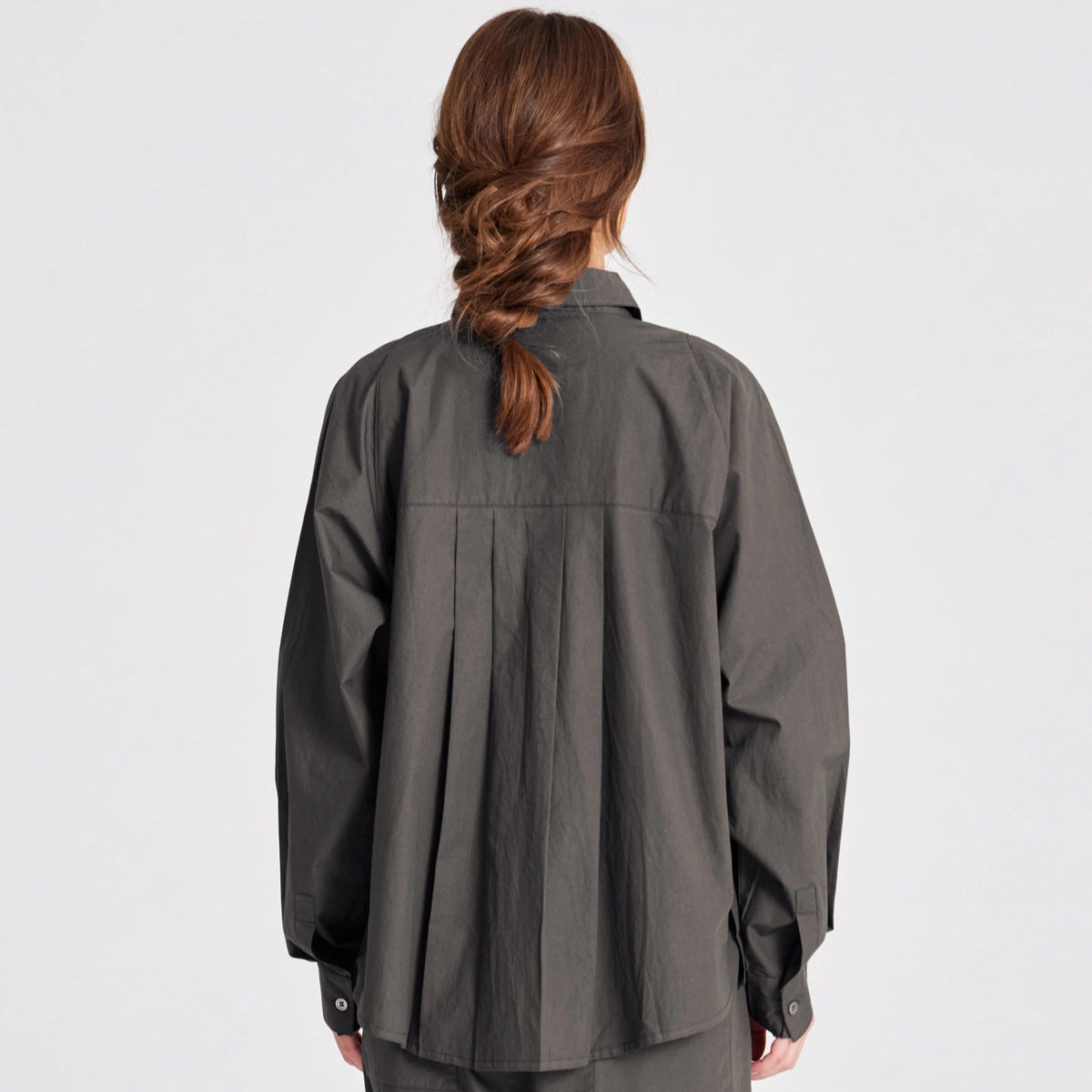 Bella er en lang skjorte med lange raglan ærmer, brystlomme samt knapper foran og på manchetter. Bella har plisseringer bagpå, slidser i siderne og er længere bagpå. Denne er i farven Beluga, som er en khaki/brun farve