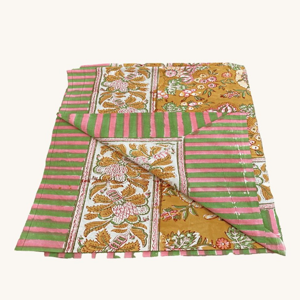 Et dug/sengetæppe med et gul blomstermønster i midten og en stribede pink og grøn kant