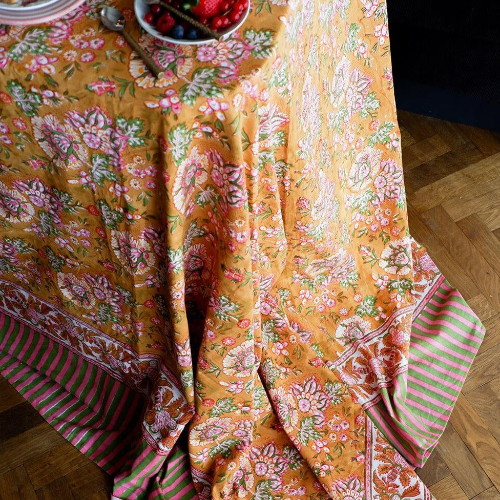 Et dug/sengetæppe med et gul blomstermønster i midten og en stribede pink og grøn kant