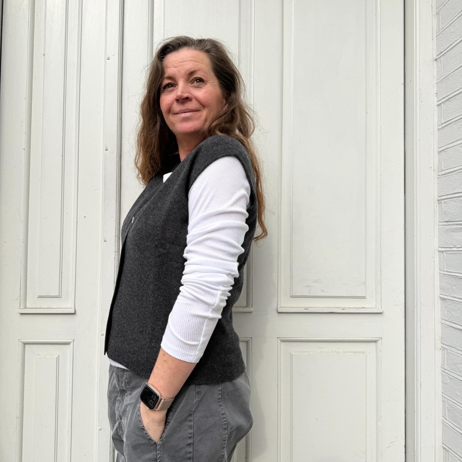 Kvinde iført mørkegrå strikvest fra Note Anecdote i merinould og cashmere med V-udskæring og perlemorsknapper.