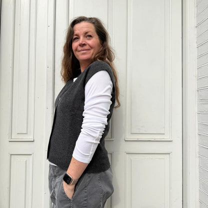 Kvinde iført mørkegrå strikvest fra Note Anecdote i merinould og cashmere med V-udskæring og perlemorsknapper.