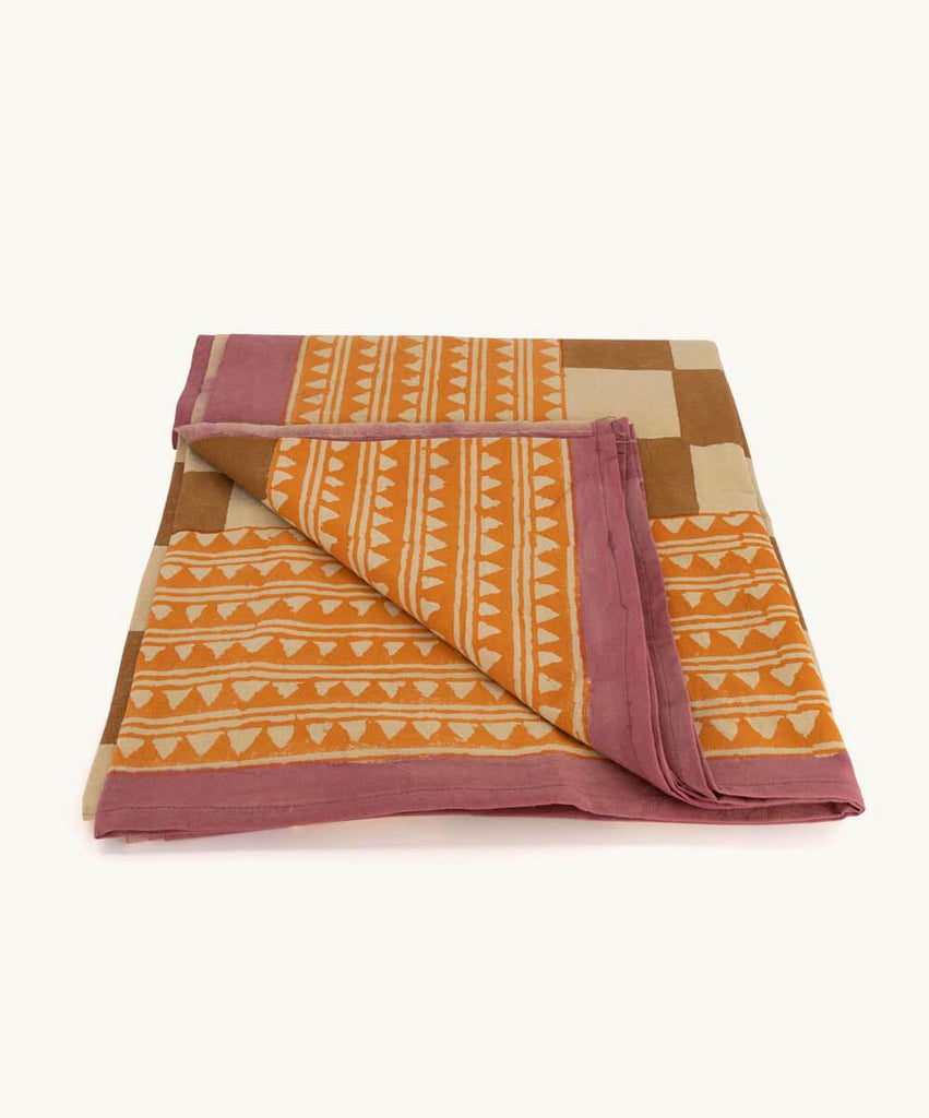 Et dug/sengetæppe med ternet mønster i beige og brun samt en orange og pink kant