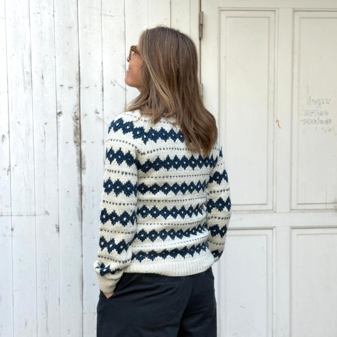 Hvid strik cardigan fra Chola med blåt strikket mønster. Trøjen er lavet af kvinder i Bolivia og er lavet i alpakauld