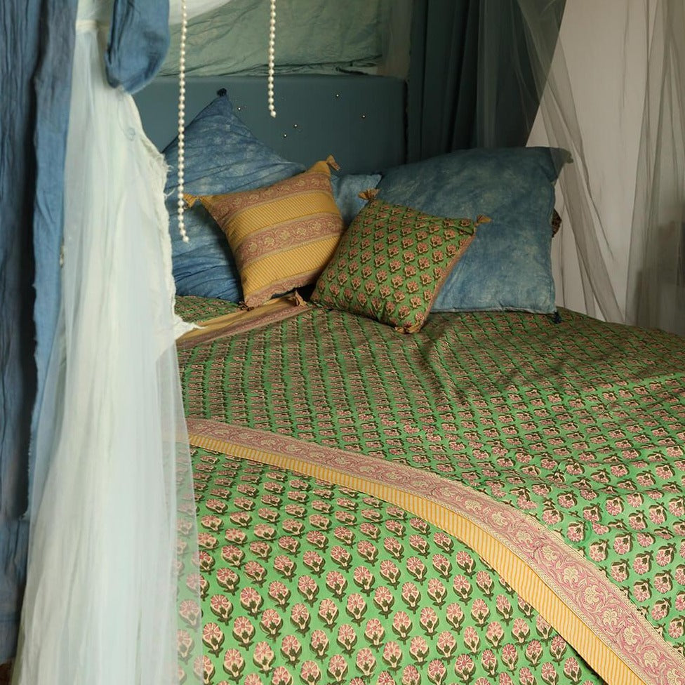 Et dug/sengetæppe med et grønt blomstermønster i midten og en lyserød og gul kant