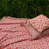 Et dug/sengetæppe med et pink og orange leopard mønster i midten og en rød mønstret kant