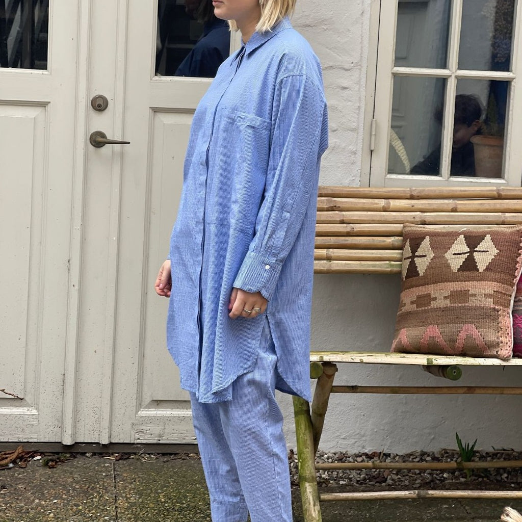 Den lange blå stribet bomuldsskjorte i er perfekt oversized hverdagsskjorte fra Frau. Skjorten er lidt længere bagpå og runder fint foran. Skjorten er gennemknappet, og er lavet i økologisk bomuldspoplin, som gør den åndbar og behagelig at have på. Størrelsen er one size