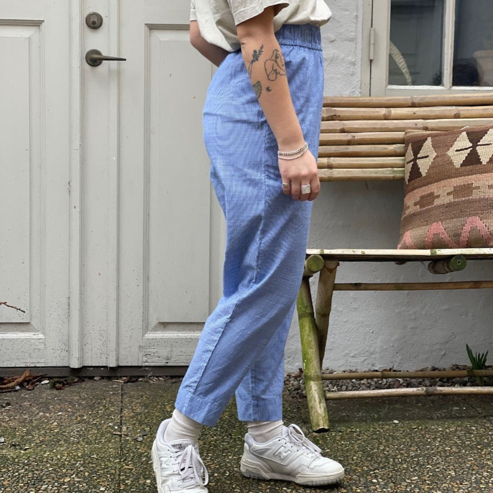 De populære oslo bukser er lavet i økologisk bomuld og har smalle ben, som gør sig godt med en løs skjorte eller strik til. Bukserne har sidelommer og en bred elastik i taljen. Bukserne er blå stribet og kommer med matchende skjorte. Lavet i åndbar økologisk bomuldspoplin.